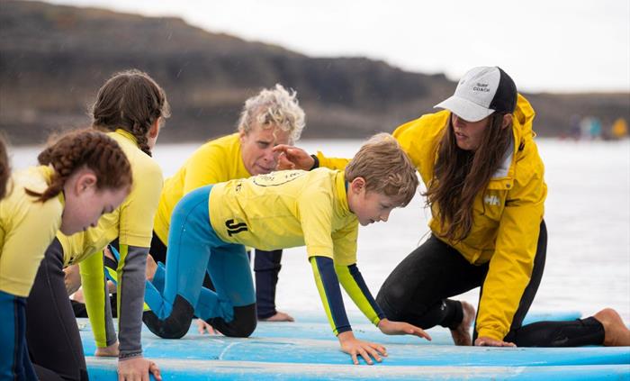 Image of students receiving a surf lesson on surf boards at the shores of the sea from an instructor.